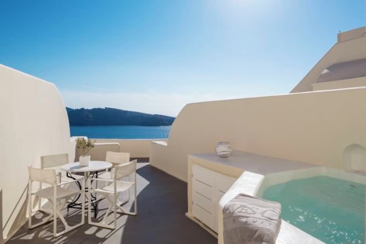 A balcony with a view of the sea, a table with chairs, and a small white cabinet.