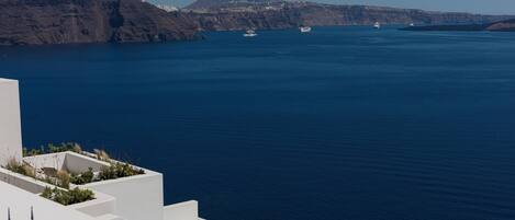 A coastal view with a white building, a clear blue sea, and distant mountains.