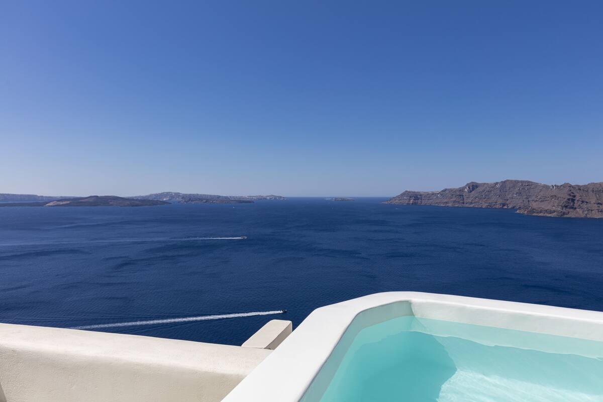 A view from a balcony with a pool, overlooking a large body of water and distant land.
