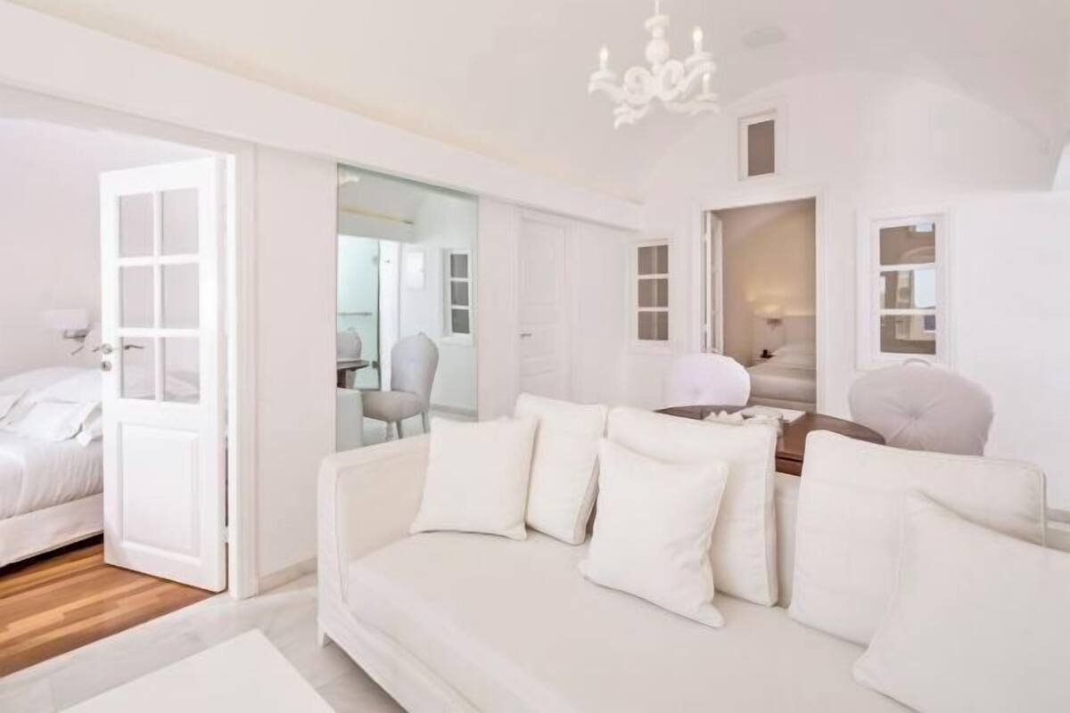 A modern, white-themed living room with a sofa, a dining table, and a chandelier.