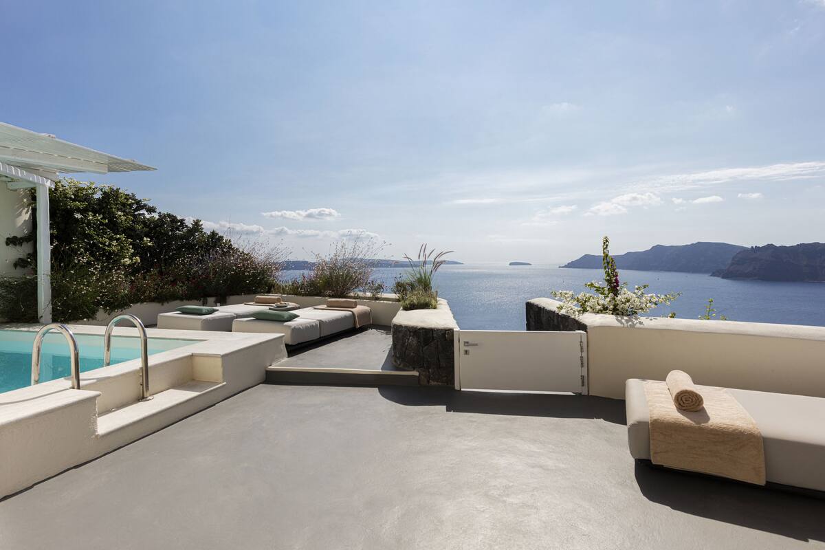A poolside area with a view of the sea, outdoor seating, and a pergola.