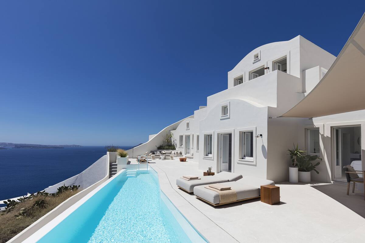 A modern white building with a pool, outdoor seating, and a view of the sea.