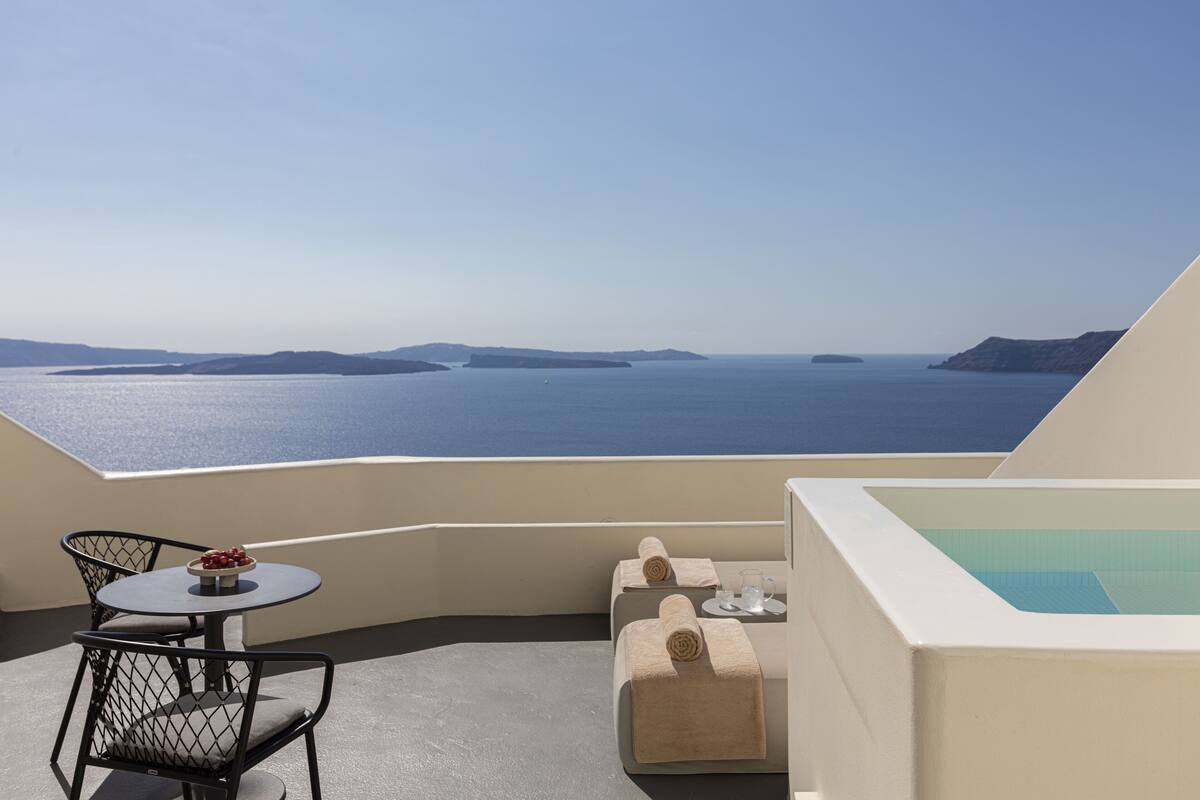 A balcony with a table, chairs, and a small pool area overlooking a body of water and distant landforms.