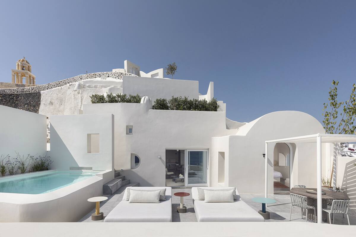 A modern white building with a pool, outdoor seating, and a view of the sea.