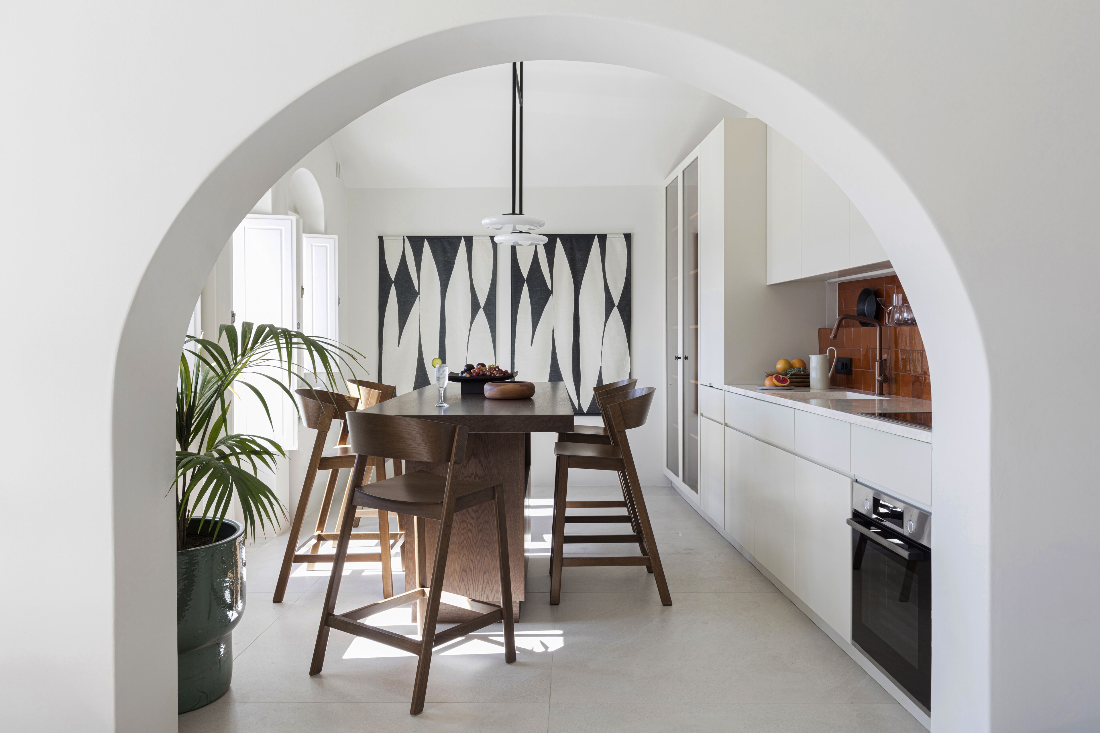 Une cuisine moderne avec des meubles blancs, une table à manger en bois et un grand tableau abstrait noir et blanc accroché au mur.