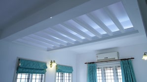 Una habitación con tragaluz, dos ventanas con cortinas, un equipo de aire acondicionado y luces fijadas a la pared.