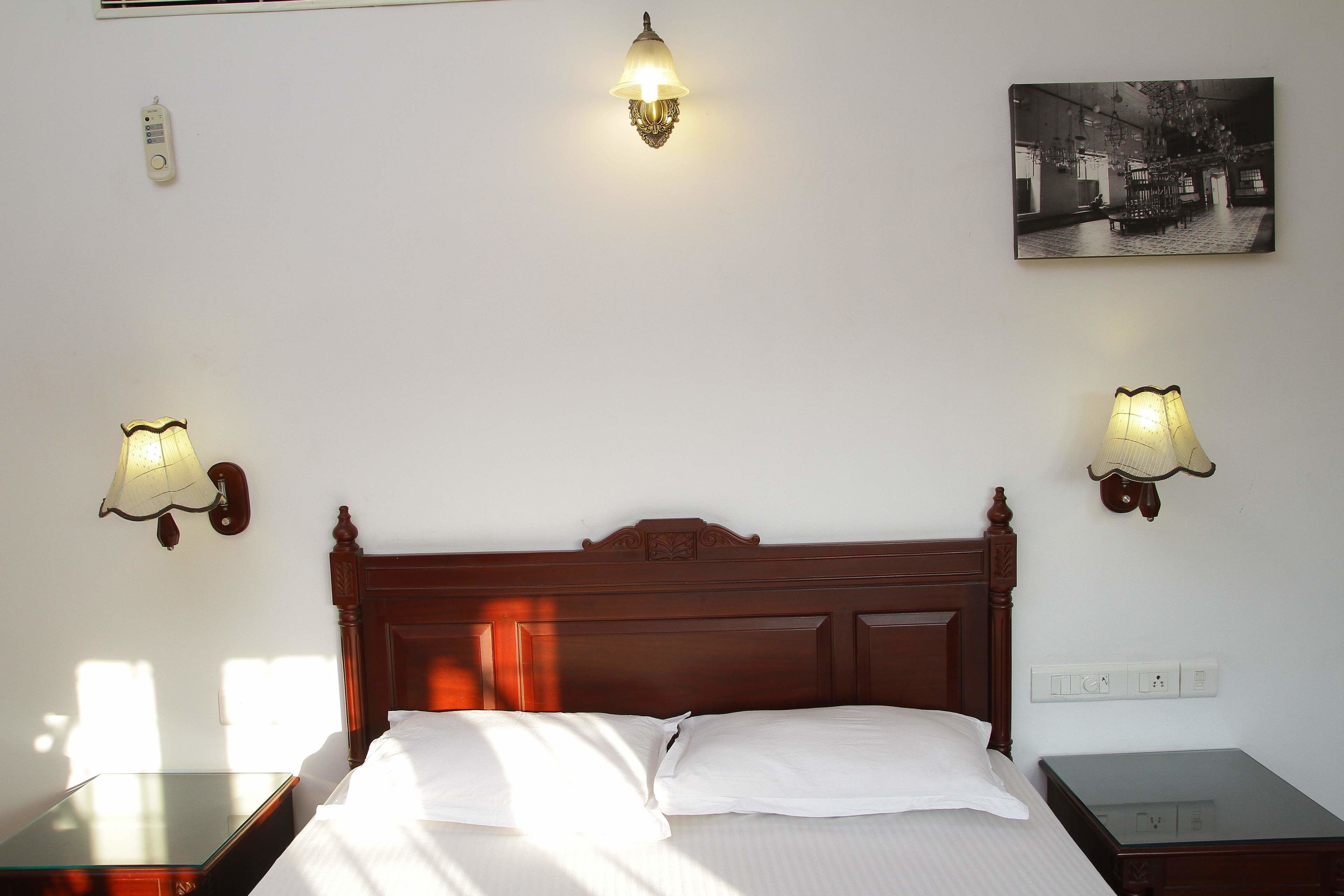 Una camera d'albergo con un letto in legno, due comodini, una lampada a parete e un quadro appeso al muro.