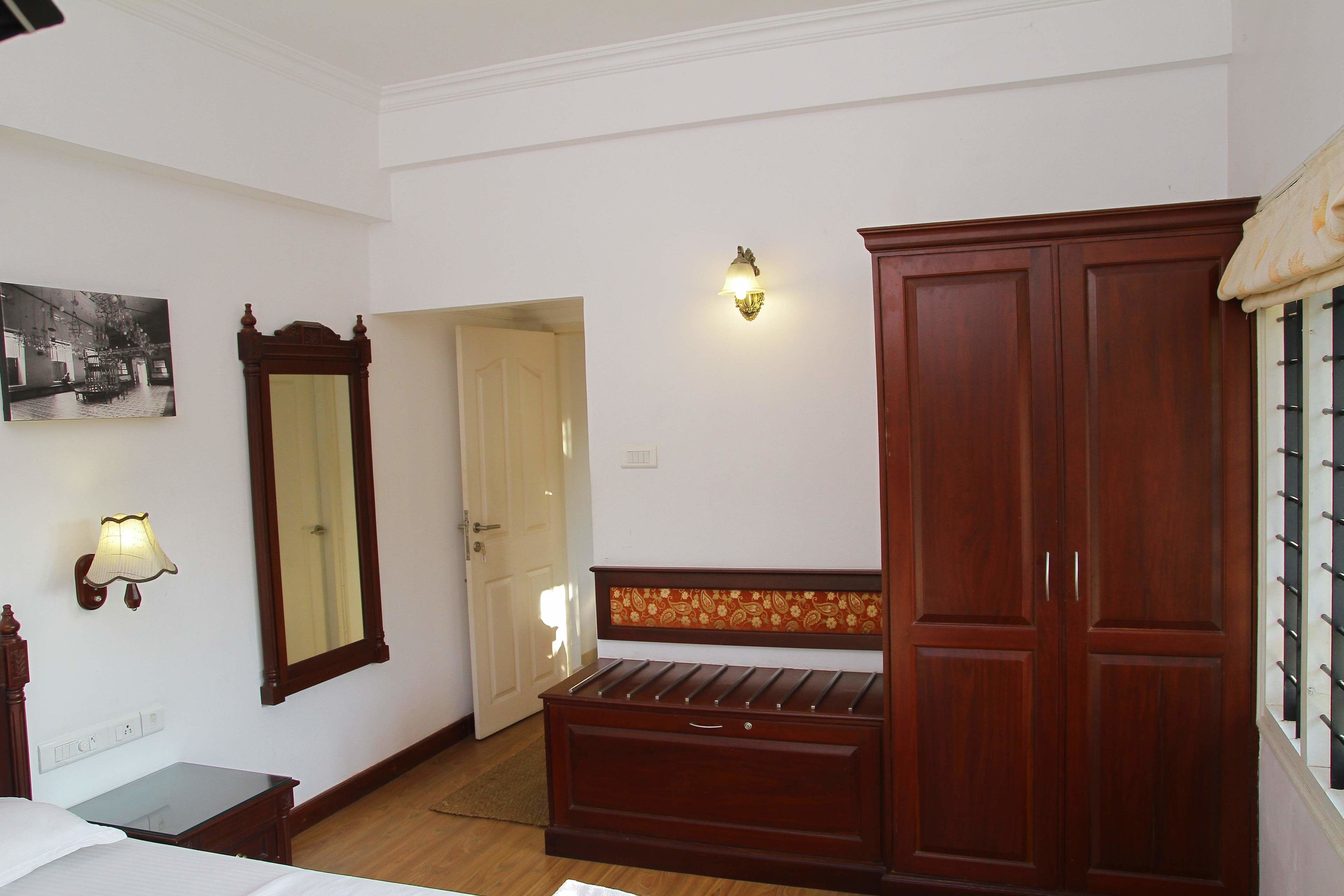 Camera d'albergo con un letto, una panca di legno, un armadio, una lampada a parete e uno specchio.