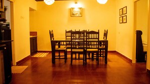 Un comedor con mesa y sillas de madera, un ventilador de techo e iluminación colgante.