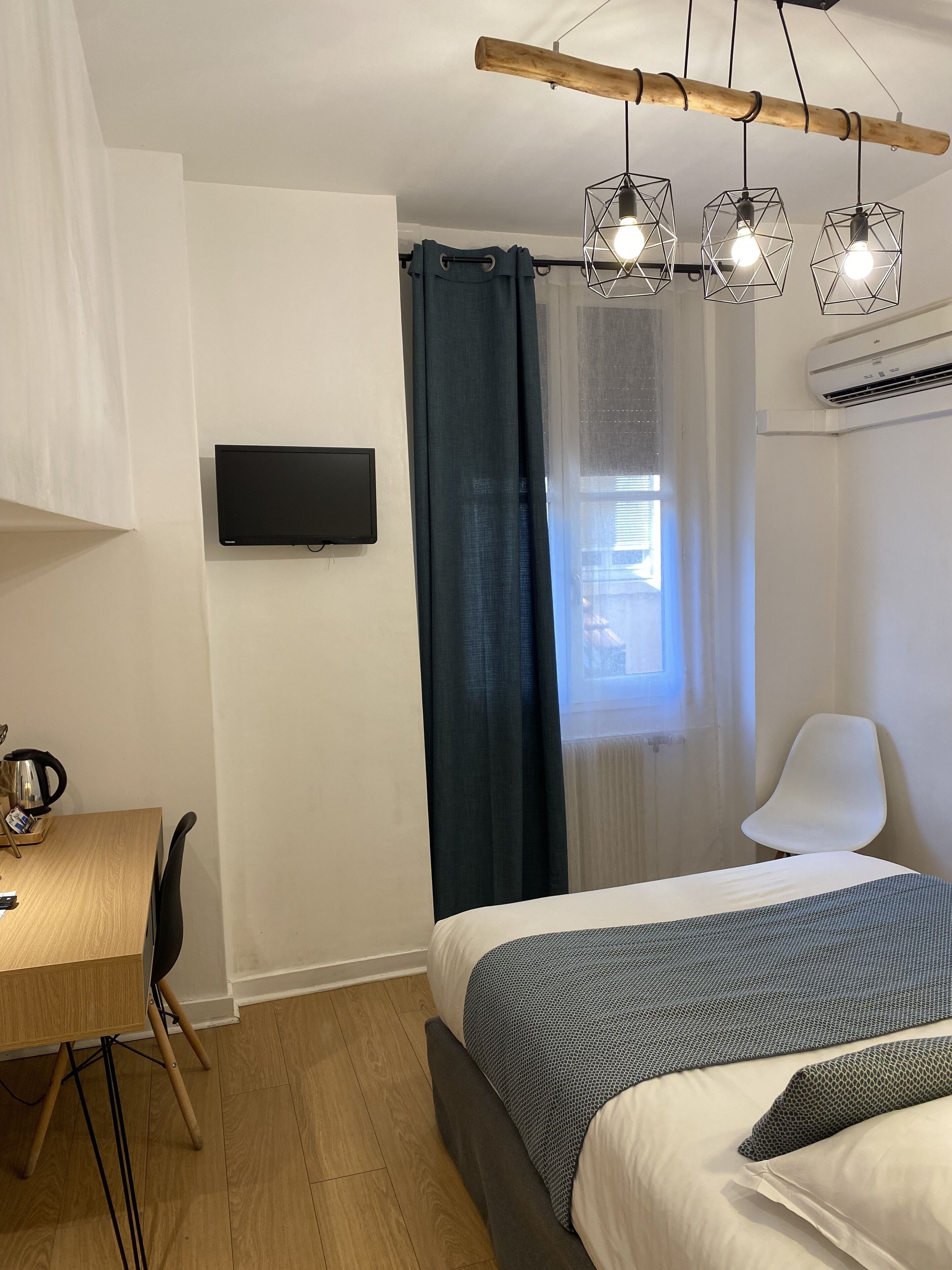 Una habitación de hotel moderna con un escritorio de madera, un televisor de pantalla plana, una cama con ropa de cama estampada y una lámpara de techo.