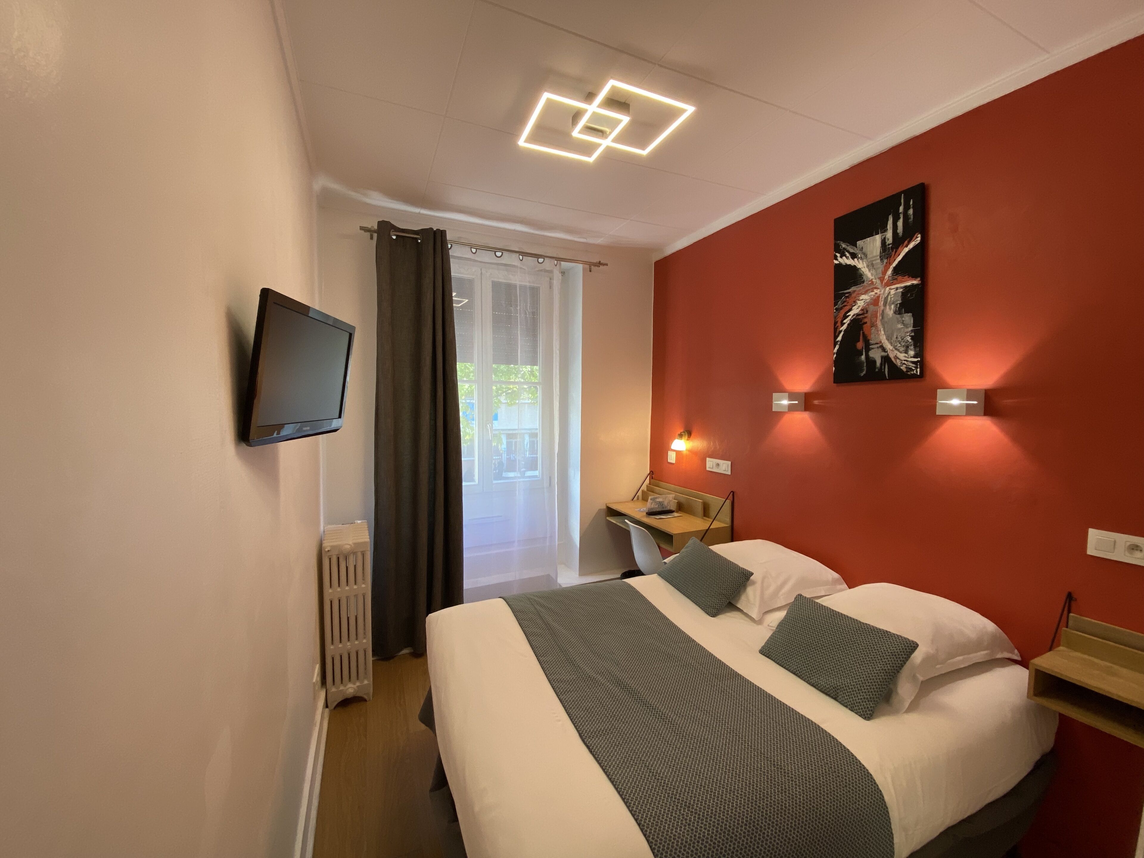 A hotel room with a bed, a desk, a chair, a TV, and a window with curtains.