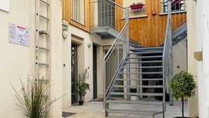 Ein schmaler Innenhof mit einem Holzgebäude, einer Metalltreppe und Topfpflanzen.