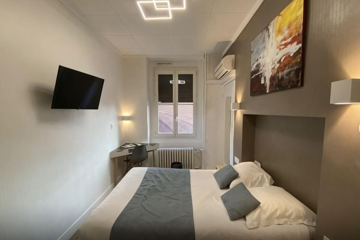 A hotel room with a bed, a desk, a chair, a television, and a window.