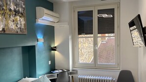 Ein modernes Schlafzimmer mit Bett, Schreibtisch und Stuhl, einem Heizkörper und einem Fenster mit Jalousien.