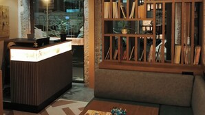 Ein Hotel-Empfangsbereich mit einem hölzernen Empfangstresen, einer Sitzecke inklusive Sofa und Couchtisch sowie einem dekorativen Holzabtrenner mit Regalen.