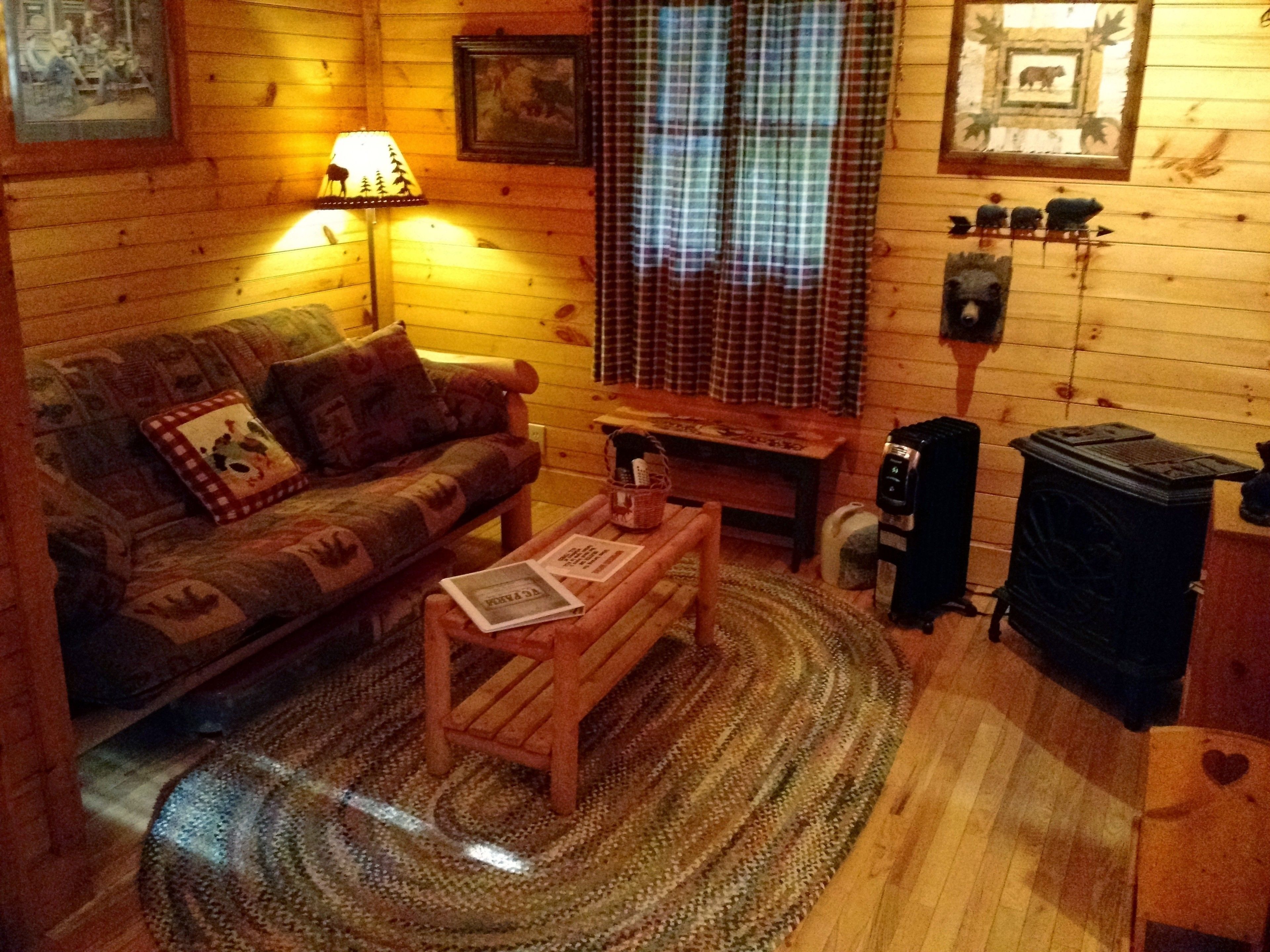 A cozy cabin interior with a wooden sofa, a small wooden table, a lamp, a fireplace, and a window with curtains.