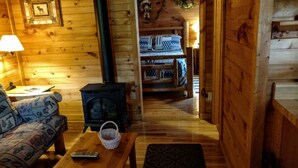 L’intérieur d’un chalet confortable, avec des murs en bois, un canapé en bois, une table sur laquelle se trouve un panier, une cheminée et un lit recouvert d’une literie à motifs.