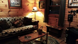 L’intérieur d’un chalet accueillant, avec un canapé en bois, une lampe, une petite table et une fenêtre avec des rideaux.