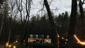 Un chalet rustique doté d’une véranda, entouré d’arbres et bordé d’un sentier de terre.