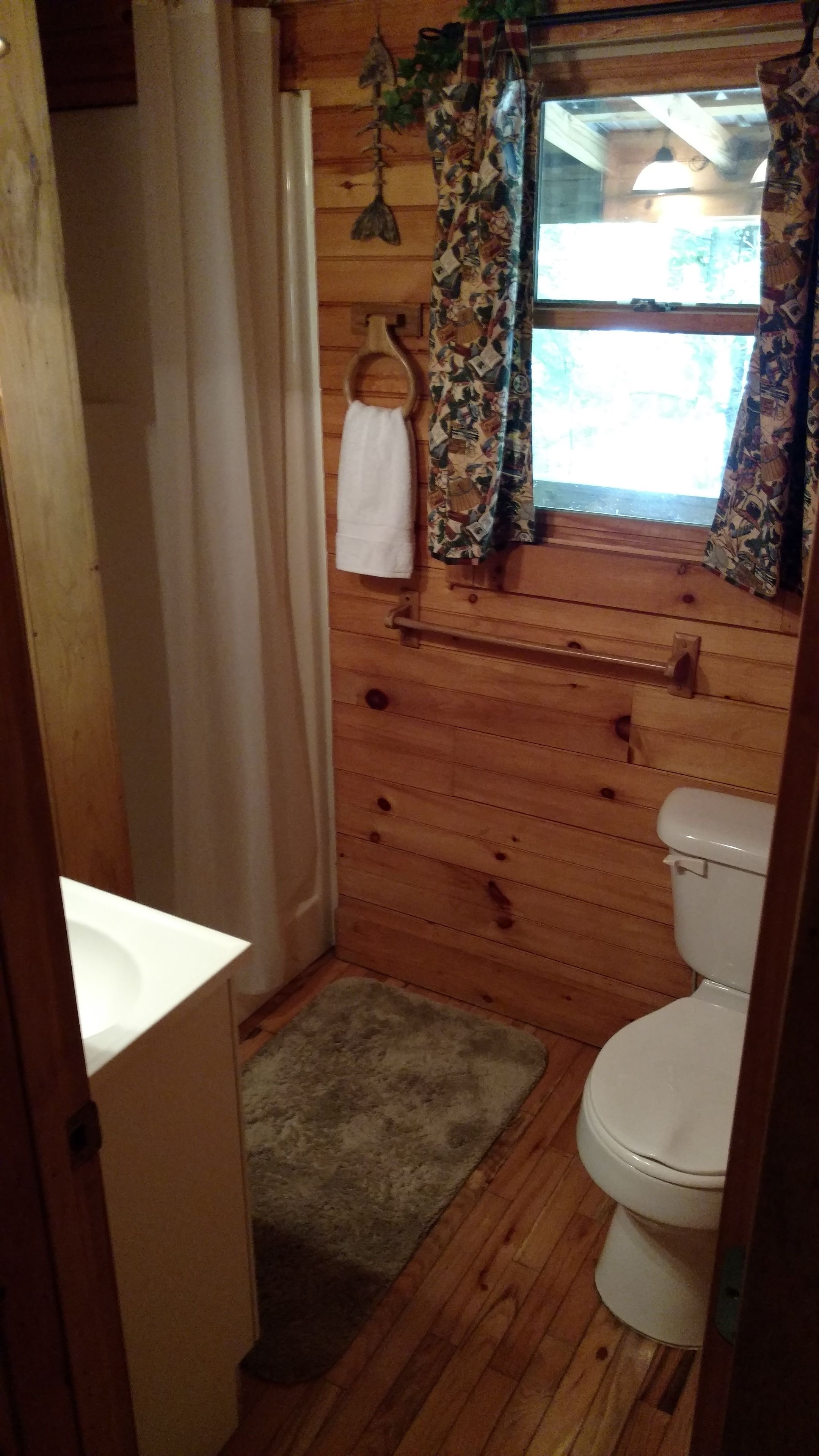 Un baño de cabaña de madera con inodoro, lavamanos y cortina de ducha.