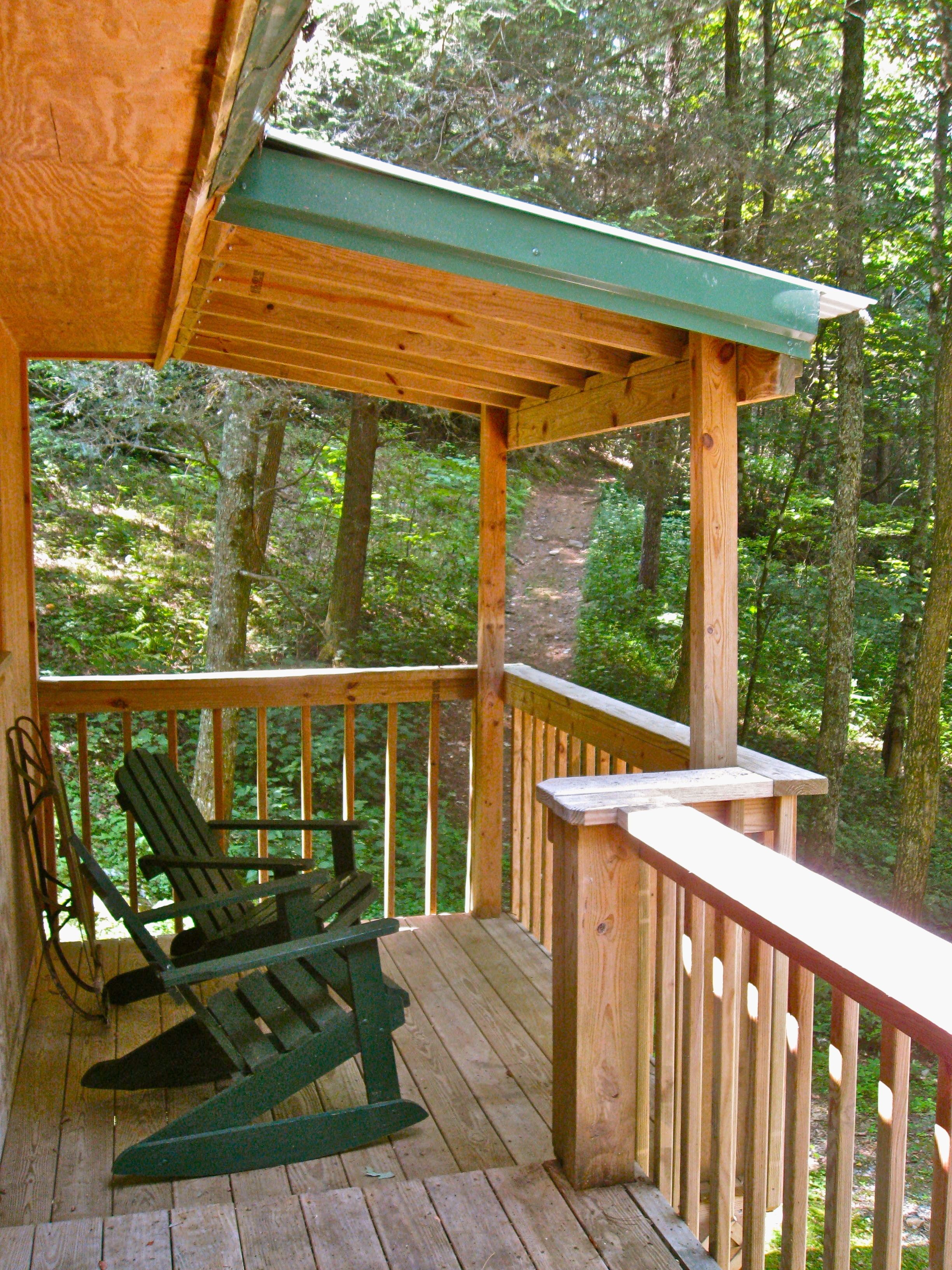 A wooden deck with a rocking chair, surrounded by a forest.