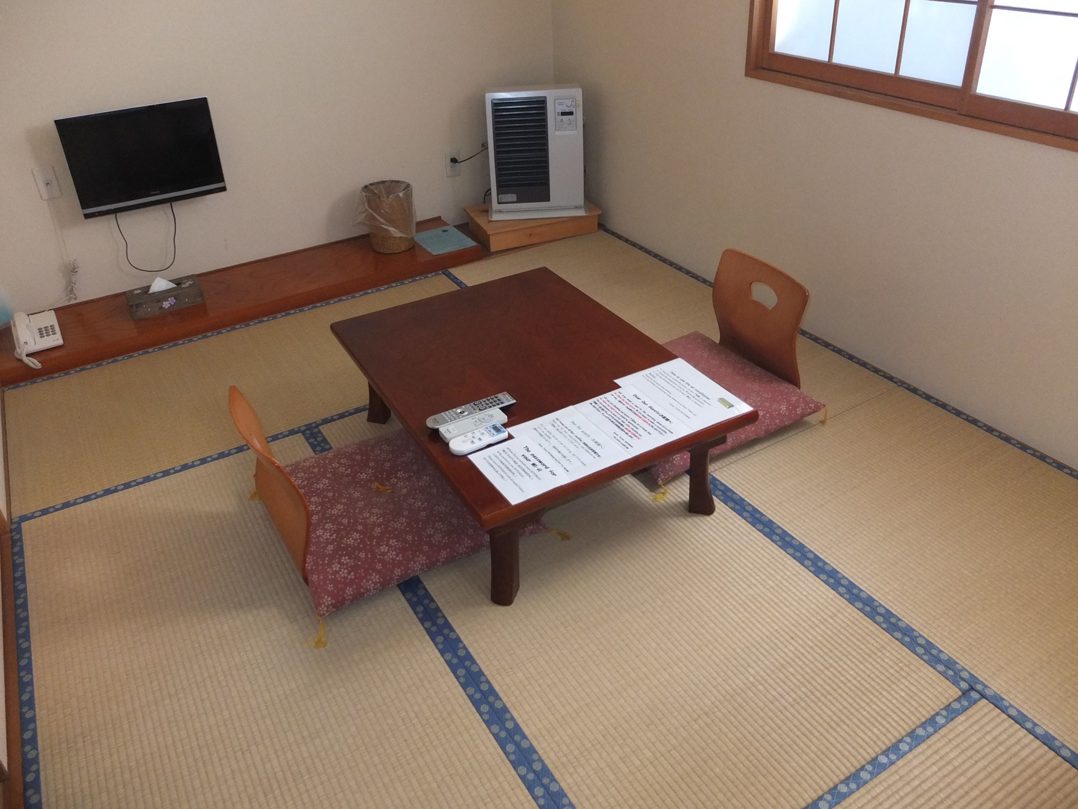 A traditional tatami mat room with a wooden table, two chairs, a TV, an air conditioner, and a telephone.