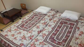 A room with a bed featuring a floral bedspread and two pillows, a wooden table with a menu, and a chair.