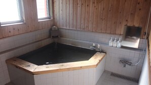 A bathroom with a wooden bathtub, tiled walls, a window, and a shower area. - Turtle Inn Nikko (Nikko)