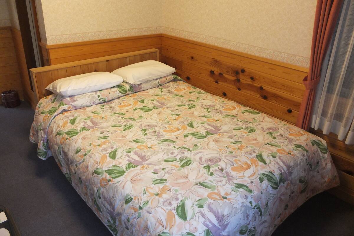 Una cama individual con edredón estampado de flores, cabecero de madera y dos almohadas.