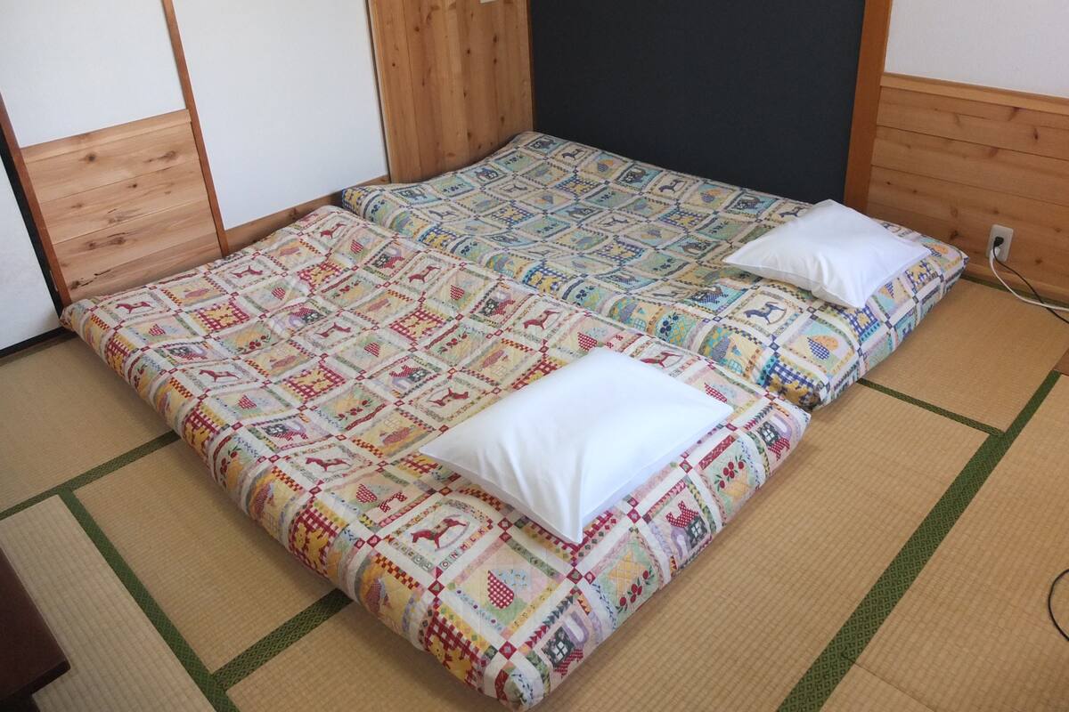 Una habitación con cabeceros de cama de madera, dos camas con colchas de colores y suelo de esteras de tatami.