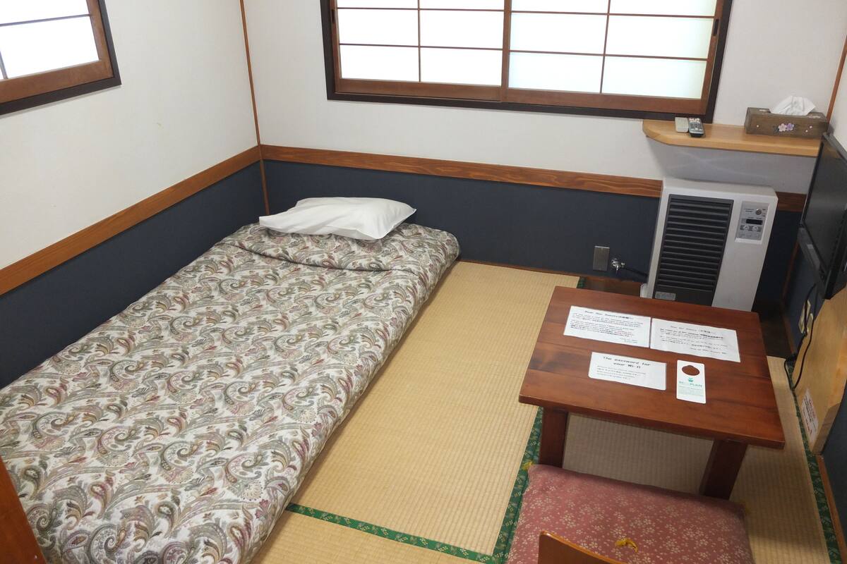 Habitación pequeña con cama, una mesita y una silla, un calentador y ventana con vistas.