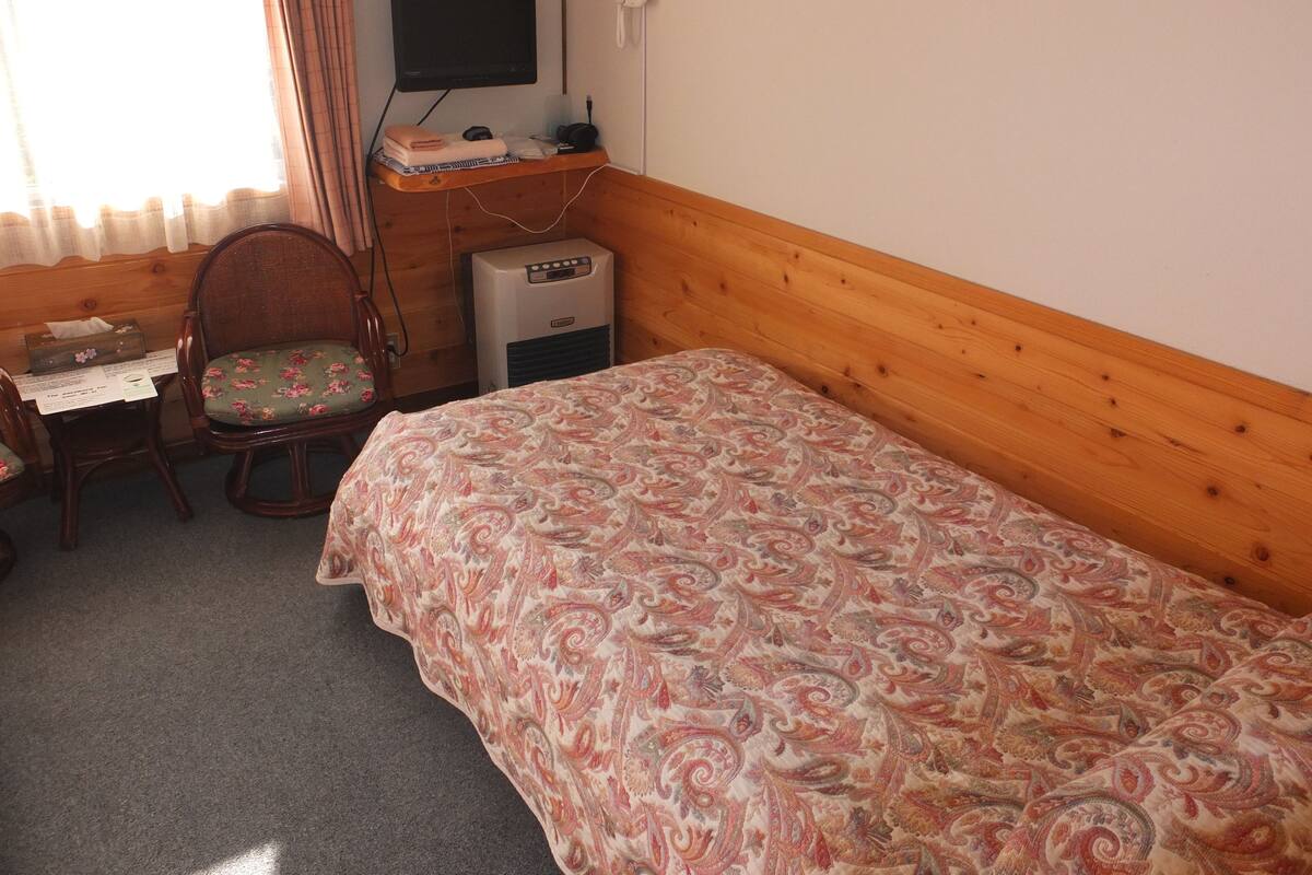 Un dormitorio con cabecera de madera, cama con colcha estampada, escritorio con silla, televisor de pantalla plana y teléfono en la pared.