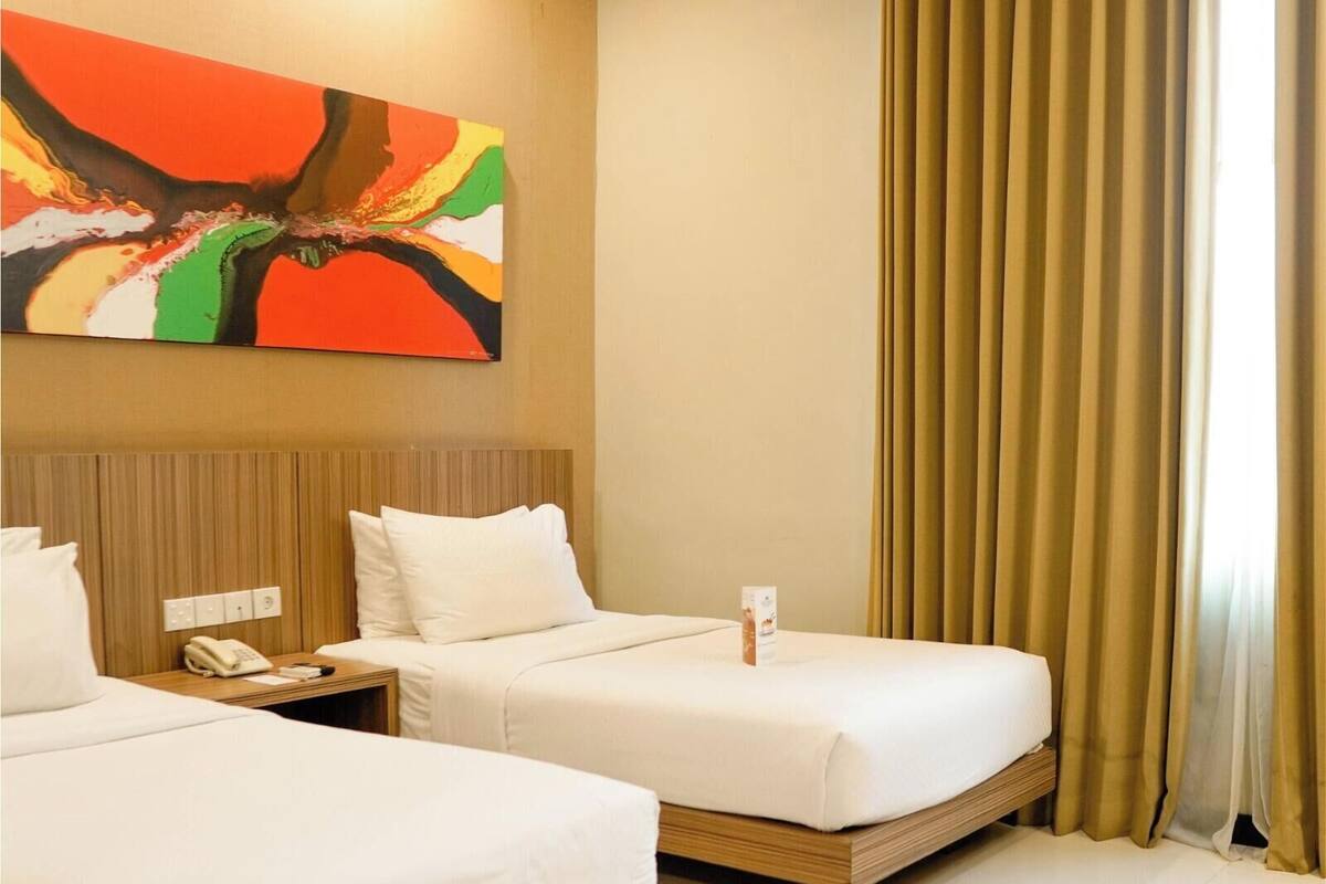 A hotel room with two beds, a wooden headboard, a painting on the wall, and a window with curtains.