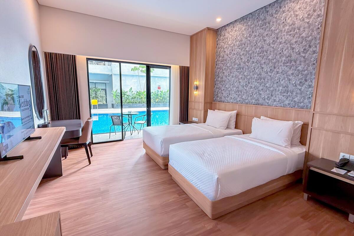A hotel room with two beds, a desk, a TV, and a view of an outdoor swimming pool.