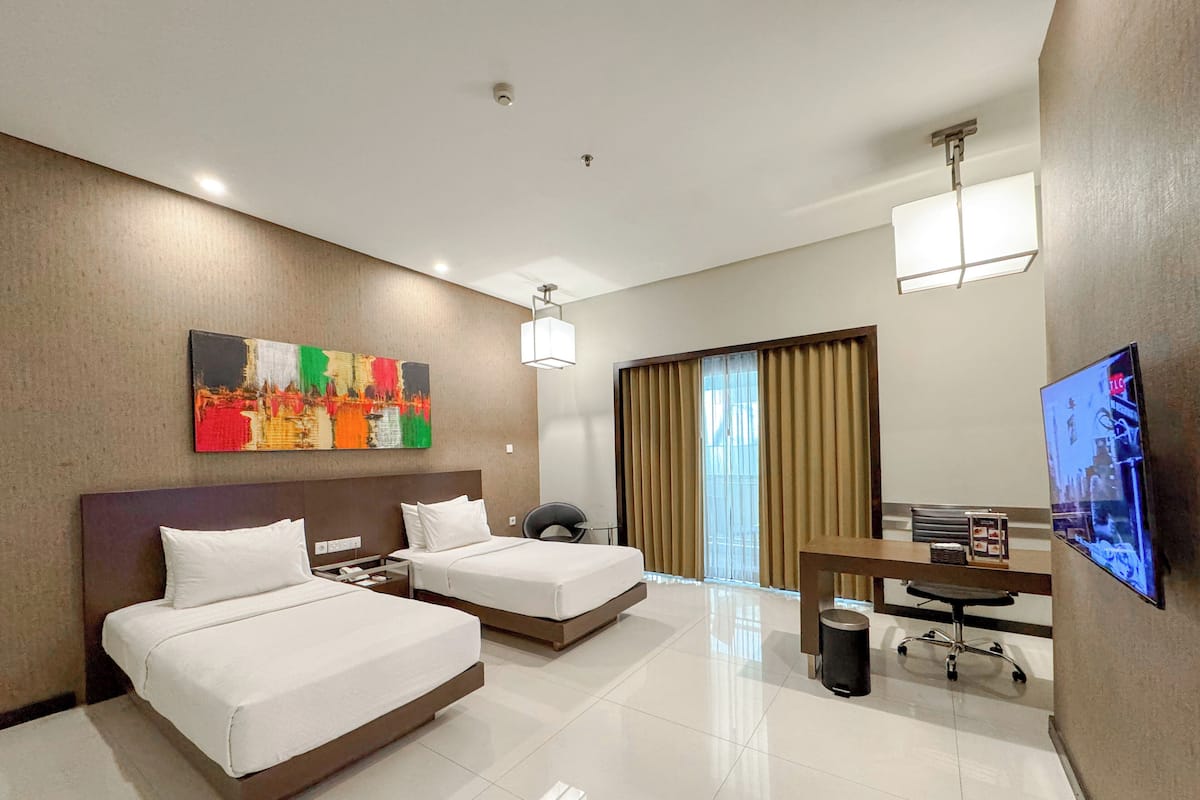 A hotel room with two beds, a desk, a chair, a TV, and a painting on the wall.