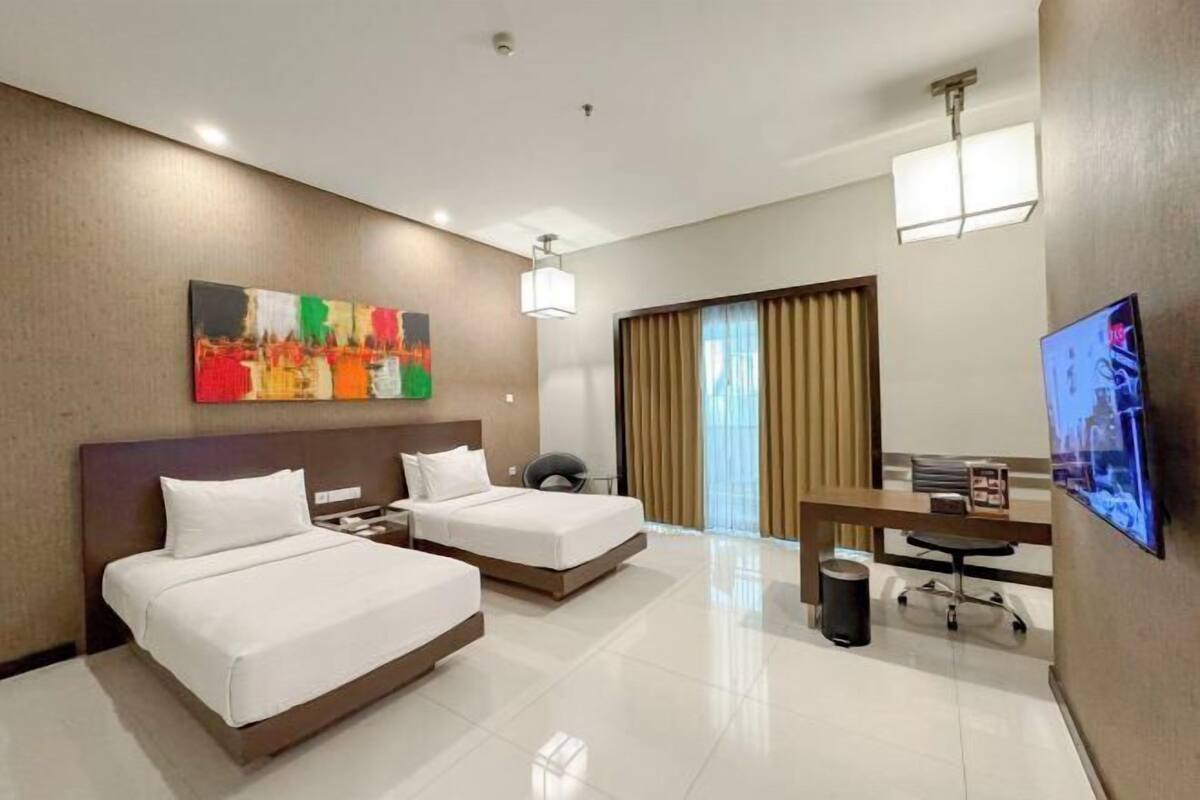 A hotel room with two beds, a desk, a chair, a television, and a painting on the wall.