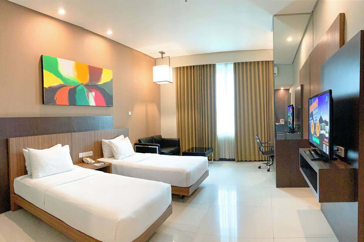 A hotel room with two beds, a TV, a desk, and a painting on the wall.