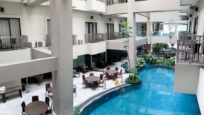 A multi-level hotel atrium with a central pool, multiple dining areas, and balconies.