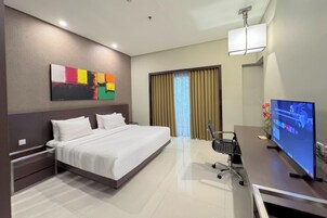 Habitación de hotel con una cama grande, un escritorio con ordenador, televisión y ventana con cortinas.