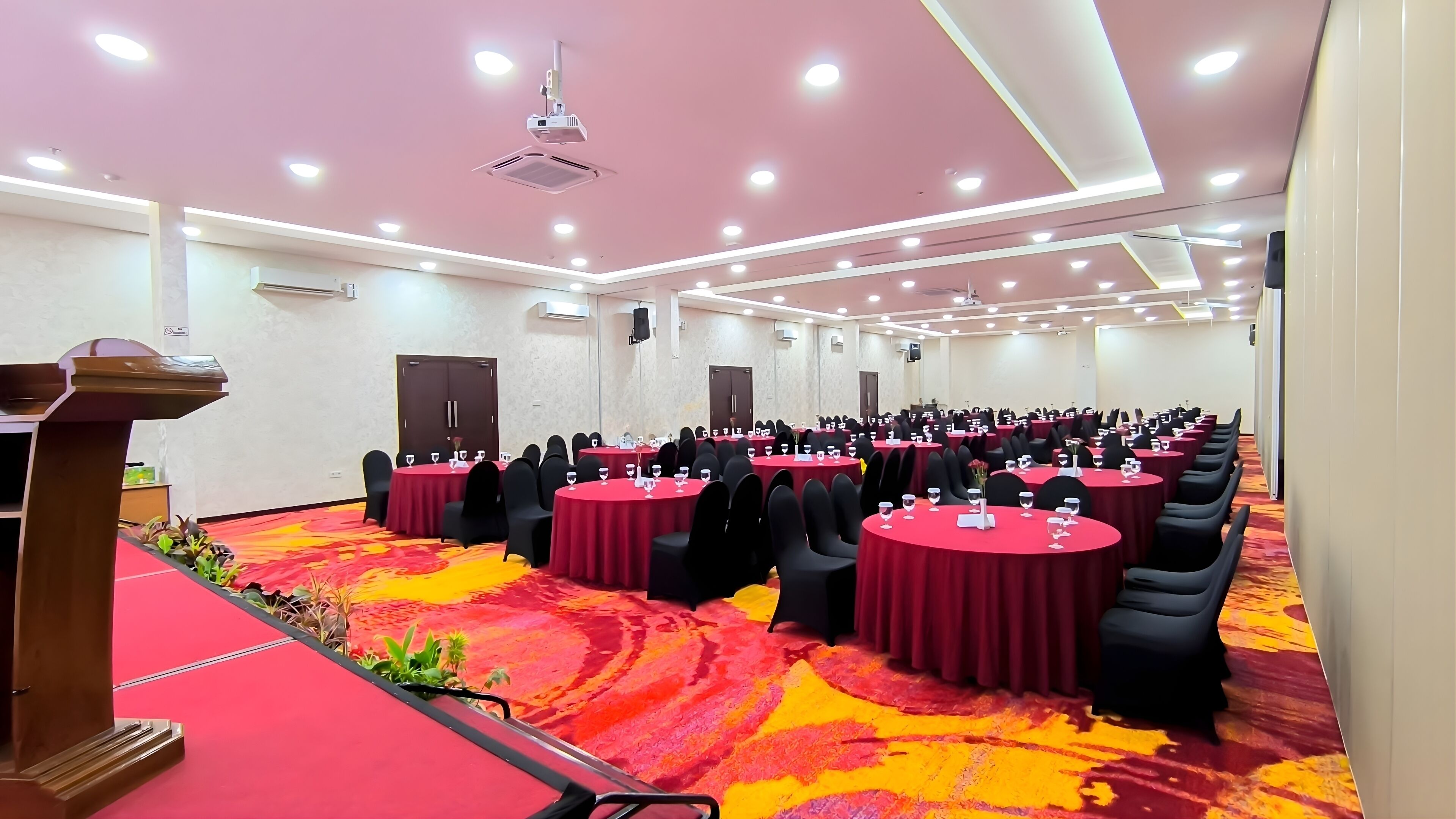 A conference room with round tables, black chairs, and a red carpet.