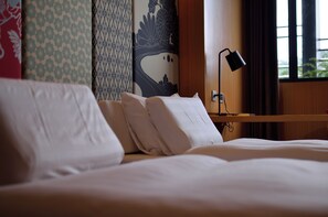 A neatly made bed with pillows, a bedside lamp, and a wall with floral and geometric patterns.