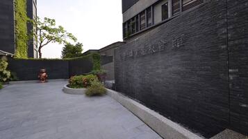 A modern building with a dark brick facade, a tree, and a statue in the courtyard.
