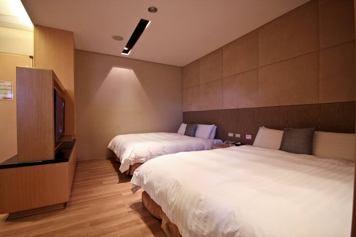 A hotel room with two beds, a wooden cabinet, and a ceiling light.