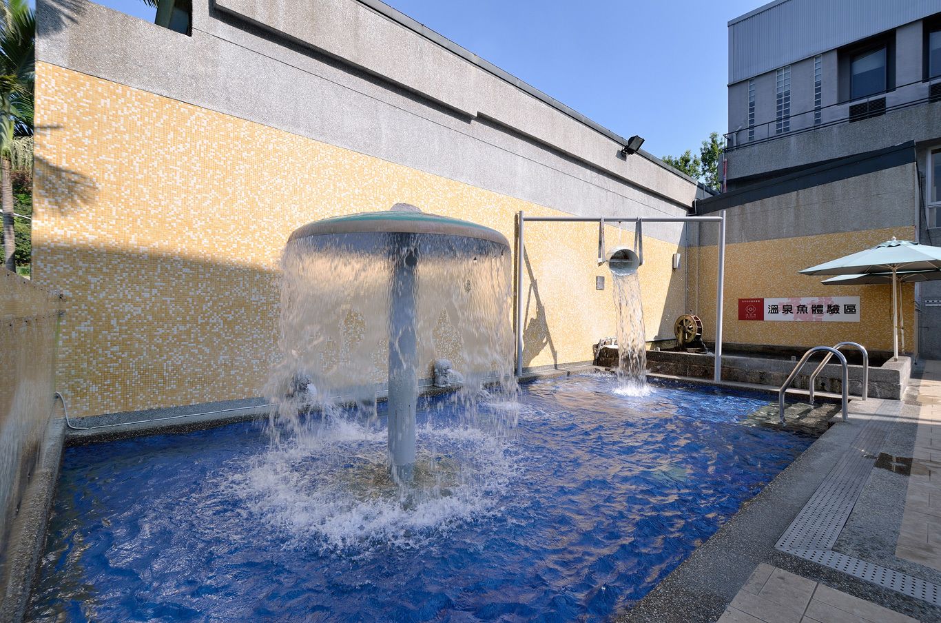 A pool area with a water fountain, a ladder, and a sign in a foreign language.
