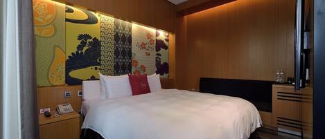 Une chambre d’hôtel avec un grand lit, une tête de lit en bois, un téléviseur à écran plat, une table de chevet avec un téléphone et un mur recouvert d’un papier peint à motifs.