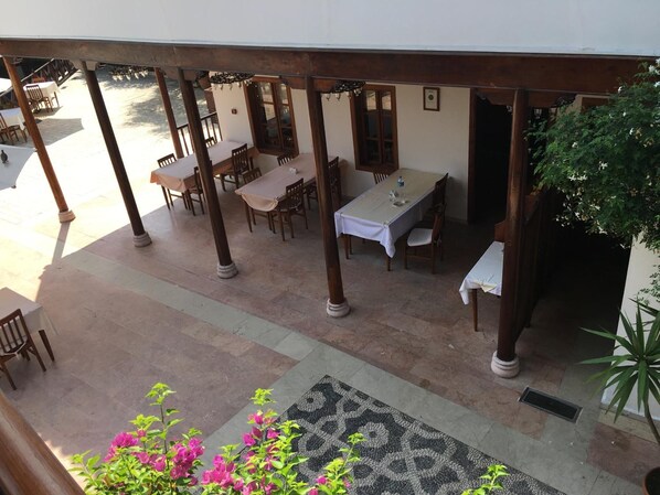 Une terrasse extérieure avec des tables et des chaises, un tapis à motifs et des plantes en pot.