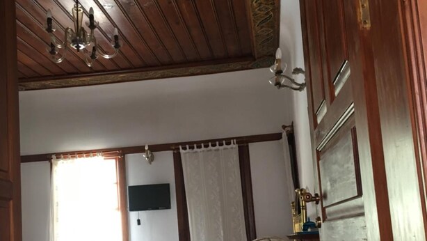 A bedroom with a wooden ceiling, a bed with a patterned bedspread, a desk with a chair, and a window with curtains. - Tekeli Konakları (Antalya)