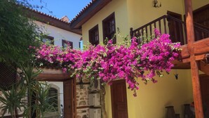 A courtyard with a yellow building, a wooden staircase, and vibrant pink bougainvillea flowers. - Tekeli Konakları (Antalya)