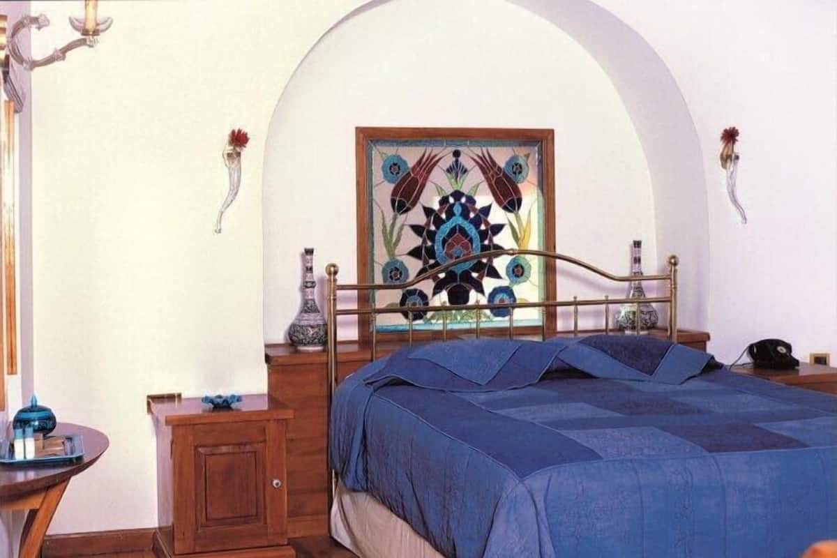 A bedroom with a bed, a wooden nightstand, a chair, a desk, and a decorative wall piece.