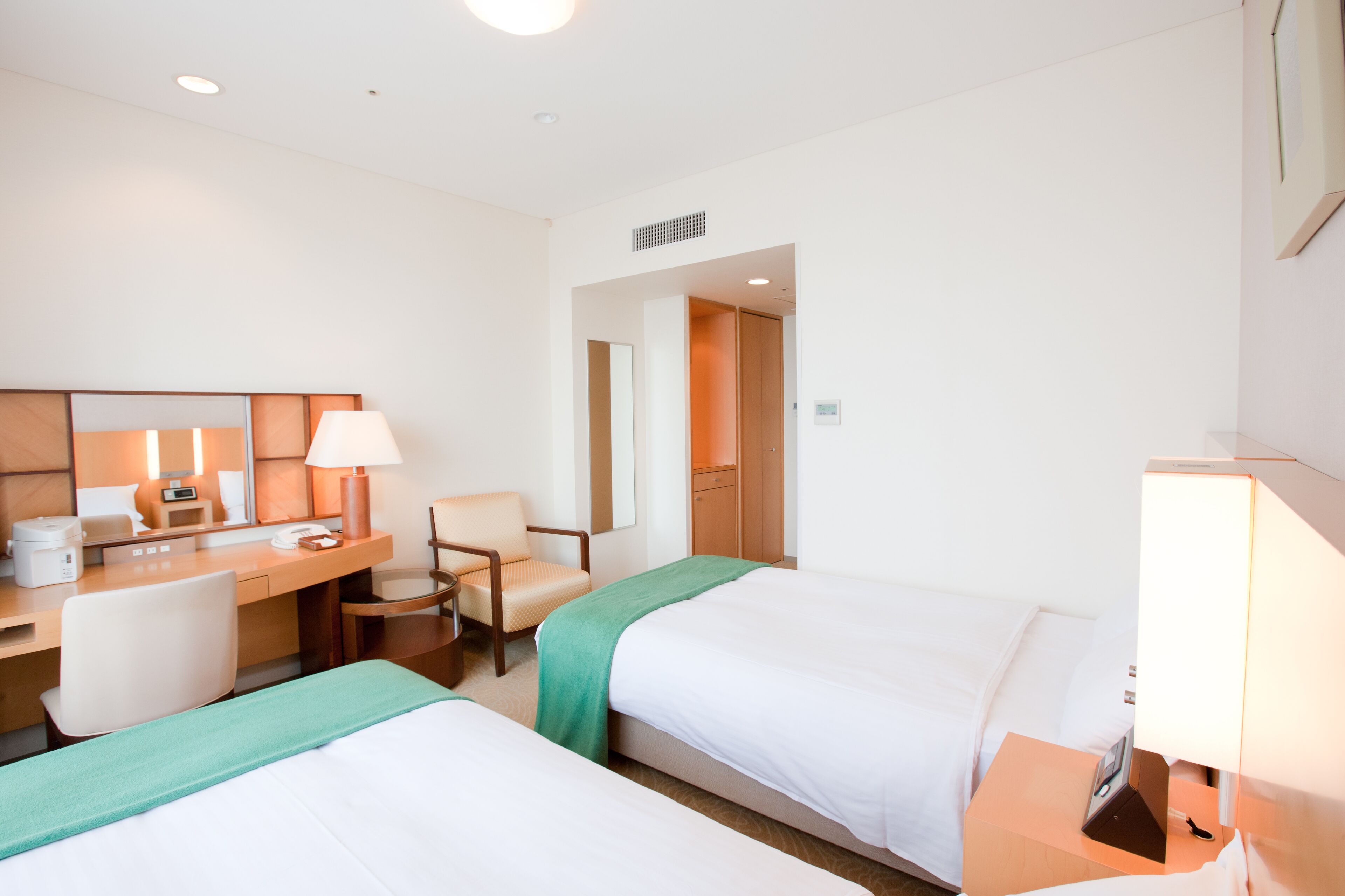 A hotel room with two beds, a desk, a chair, a lamp, and a mirror.